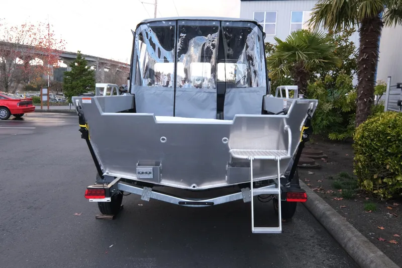 Slide: The Image of 2026 Hewescraft 180 Sportsman boat rear view, parked outdoors with trees and buildings nearby. - 5