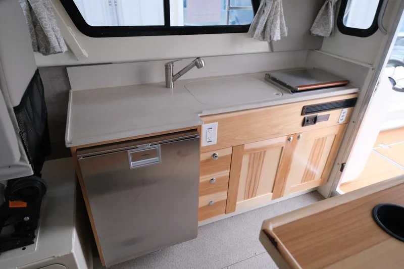 Slide: The Image of 2025 Hewescraft 290 Adventure boat interior with kitchenette, featuring sink, fridge, and wooden cabinetry. - 15