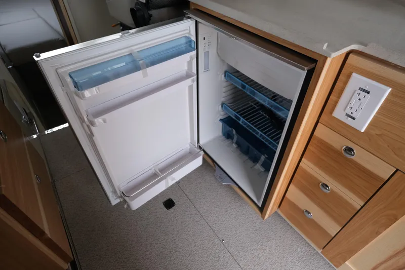 Slide: The Image of Open refrigerator inside 2025 Hewescraft 290 Adventure boat, featuring wooden cabinetry and electrical outlet. - 16