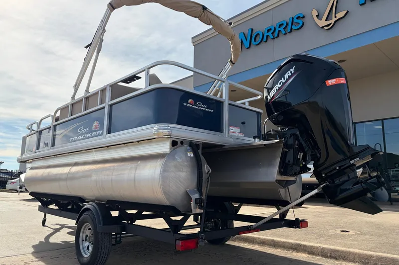 Slide: The Image of 2025 Sun Tracker Bass Buggy 18 DLX pontoon boat with Mercury engine, parked outside dealership. - 7