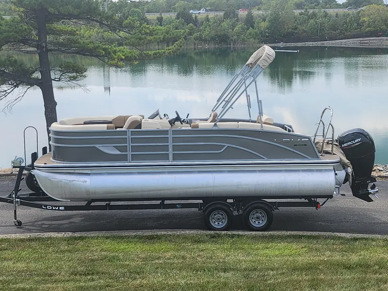 Slide: The Image of 2022 Lowe SS 210 CL pontoon boat on trailer by a serene lake. - 0