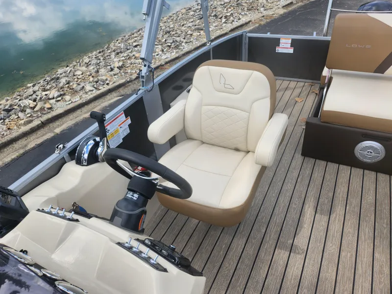 Slide: The Image of 2022 Lowe SS 210 CL boat interior with beige seating and steering wheel, near rocky shoreline. - 12