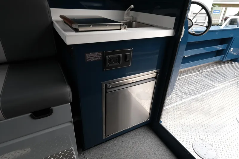 Slide: The Image of 2025 Hewescraft 270 Alaskan interior with sink, compact fridge, and steering wheel. - 15