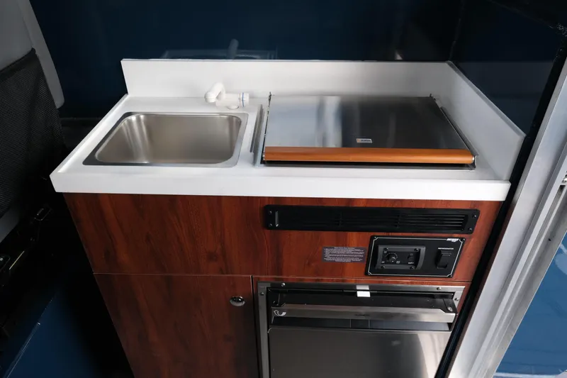 Slide: The Image of 2026 Hewescraft 250 Pacific Explorer kitchenette with sink and stove, featuring wood finish. - 13