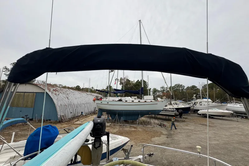 Slide: The Image of 1992 Hunter 33.5 sailboat in a boatyard, surrounded by other vessels and storage sheds. - 26