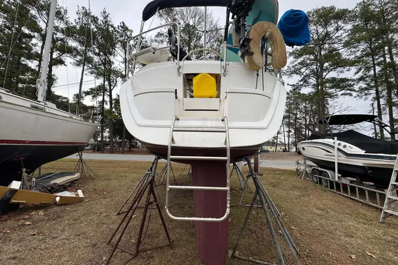 Slide: The Image of Hunter 33.5 sailboat from 1992 on stands, rear view with ladder, surrounded by trees. - 4