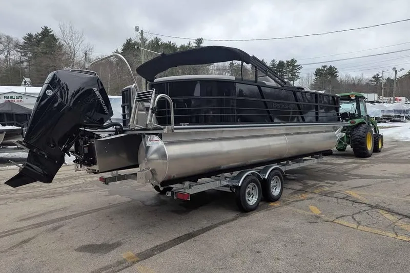 Slide: The Image of 2026 Berkshire 24RFX LE pontoon boat on trailer, parked outdoors near trees. - 2