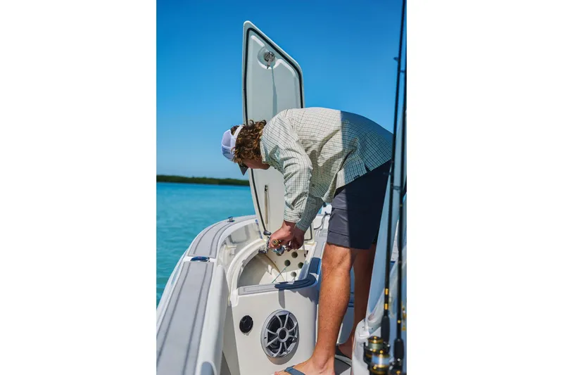 Slide: The Image of Man inspecting storage on 2026 Mako 24 APEX boat in sunny waters. - 62