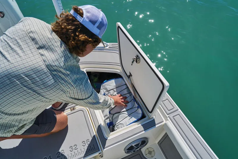 Slide: The Image of Person accessing storage compartment on 2026 Mako 24 APEX boat in sunny waters. - 70