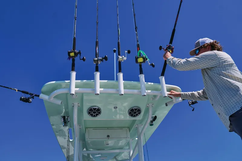 Slide: The Image of Man organizing fishing rods on Mako 24 APEX boat, 2026 model, under clear blue sky. - 74