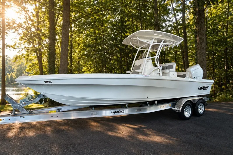Slide: The Image of 2026 Mako 24 APEX boat on trailer in a wooded area, sunlight filtering through trees. - 96