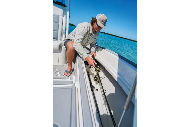 Slide: The Image of Man organizing fishing rods on a 2026 Mako 24 APEX boat in clear blue waters. - 60