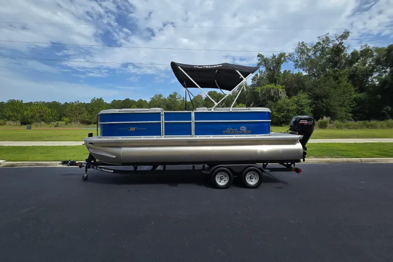 Slide: The Image of 2026 Sun Tracker Party Barge 20 DLX pontoon boat on trailer, parked outdoors. - 2