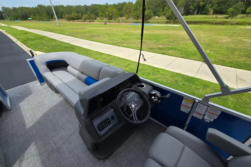 Slide: The Image of 2026 Sun Tracker Party Barge 20 DLX interior with steering console and seating, set against a grassy landscape. - 4