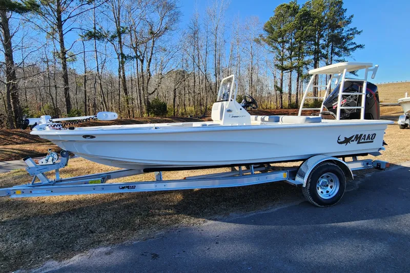 The Image of 2026 Mako 18 Pro Skiff boat on trailer, parked outdoors near trees. - 0