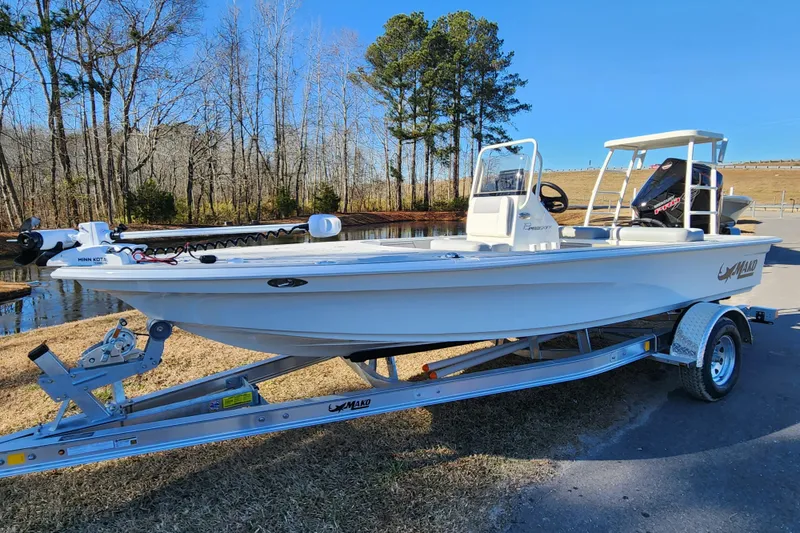 Slide: The Image of 2026 Mako 18 Pro Skiff boat on trailer by a lake, surrounded by trees. - 1