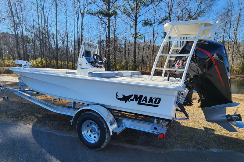 Slide: The Image of 2026 Mako 18 Pro Skiff boat on trailer, parked outdoors near trees. - 2