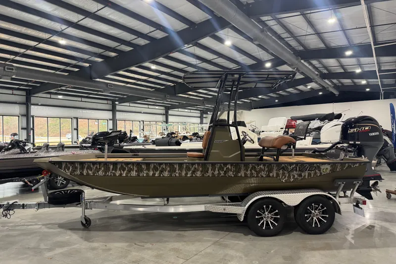 Slide: The Image of 2026 Avid 20 Rogue CC boat in showroom, featuring camouflage design and dual-axle trailer. - 17