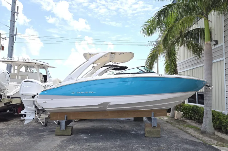 The Image of 2022 Regal LX6 boat in blue and white, displayed outdoors near palm trees. - 0