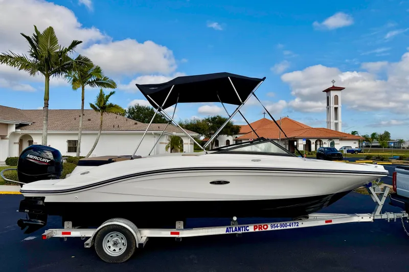 The Image of 2022 Sea Ray SPX 210 Outboard boat on trailer, parked near palm trees and buildings. - 0