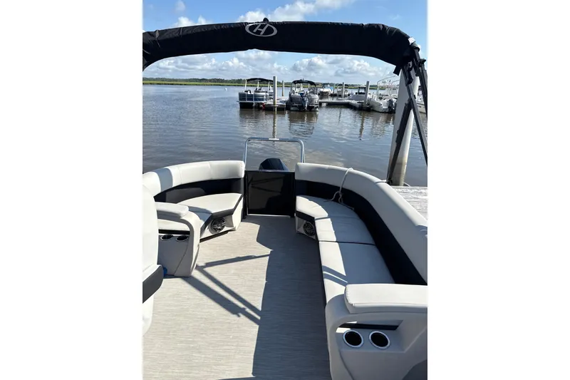 Slide: The Image of 2024 Harris Breeze 230 pontoon boat interior with spacious seating and cup holders, docked by the water. - 4