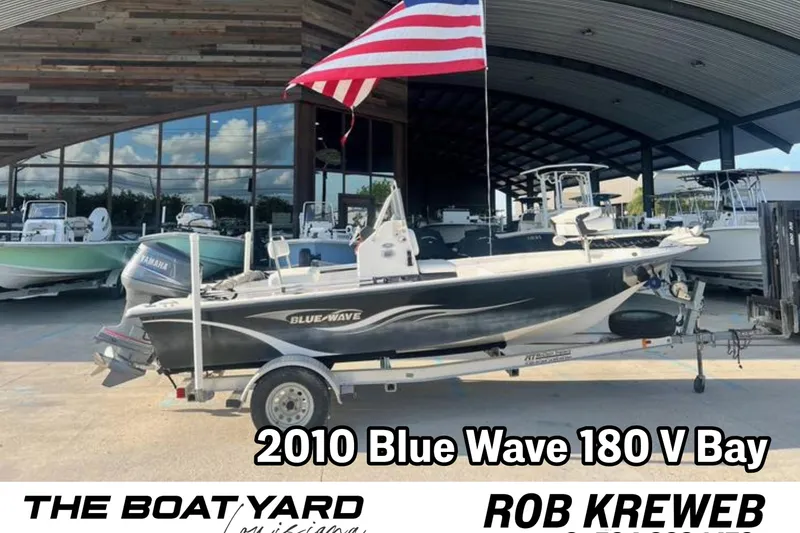 The Image of 2010 Blue Wave 180 V Bay boat on trailer with American flag, dealership background. - 0