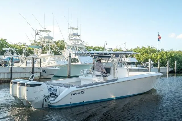 Slide: The Image of 2015 Bahama 34 boat docked, featuring triple outboard engines, with other boats in the background. - 6