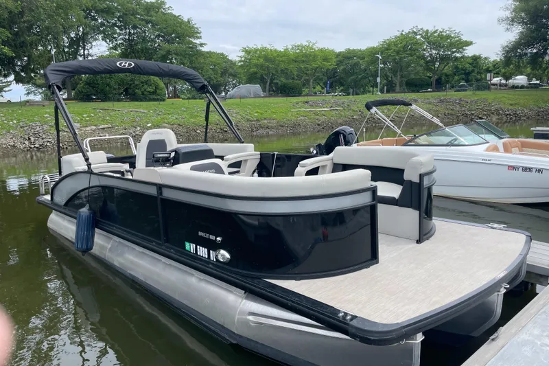 The Image of 2024 Harris Breeze 230 pontoon boat docked on a calm lake with lush greenery. - 1