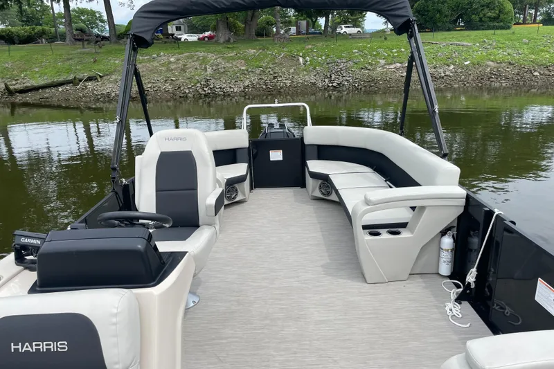 Slide: The Image of 2024 Harris Breeze 230 pontoon boat interior with seating and steering console on a calm river. - 6