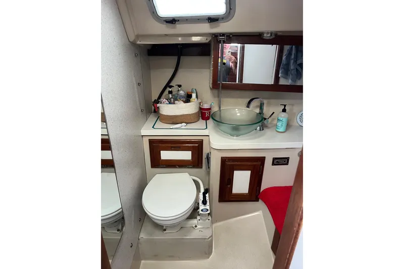 Slide: The Image of Catalina 36 MK1 1986 yacht bathroom with toilet, glass sink, and wooden cabinets. - 12