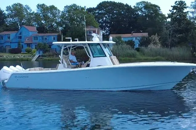 Slide: The Image of 2019 Sailfish 360 CC boat on calm water near shoreline with houses in the background. - 2