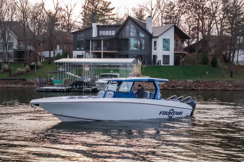 The Image of 2026 Fountain 38 SCX boat cruising on a lake near modern lakeside homes. - 2