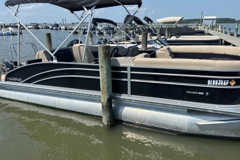 The Image of 2024 Harris HCX23 pontoon boat docked at marina, featuring sleek black design and comfortable seating. - 1