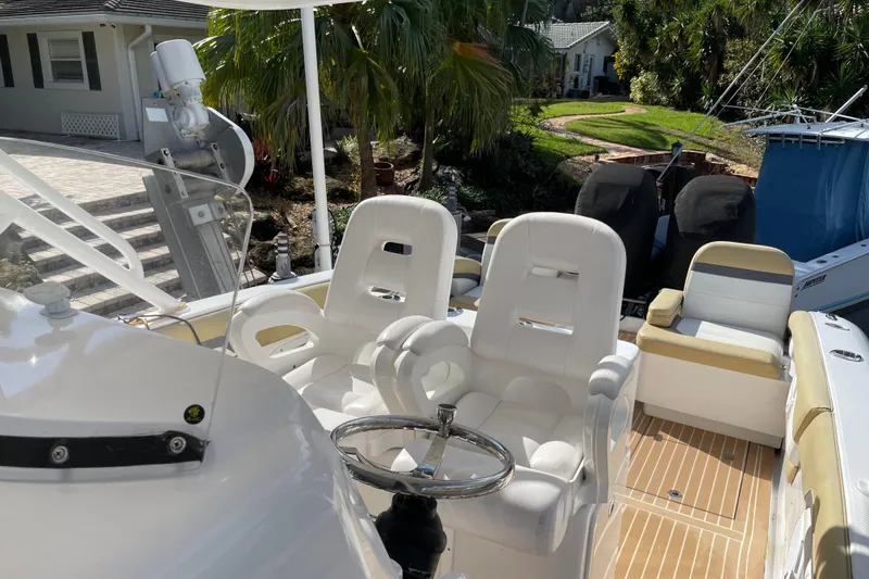 Slide: The Image of 2014 Powerplay Powerboats 35 Open with white seating and steering wheel, docked near lush greenery. - 19