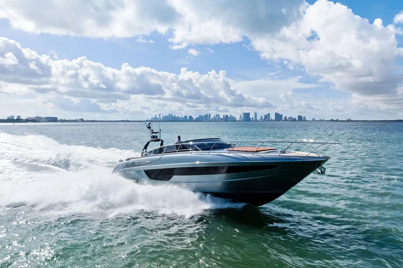 Slide: The Image of 2021 Riva 56 Rivale yacht cruising on open water with city skyline in background. - 0