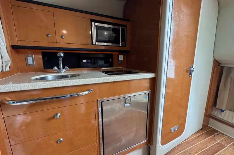 Slide: The Image of 2009 Chaparral Signature 290 boat interior with kitchenette, featuring sink, microwave, and wooden cabinetry. - 12