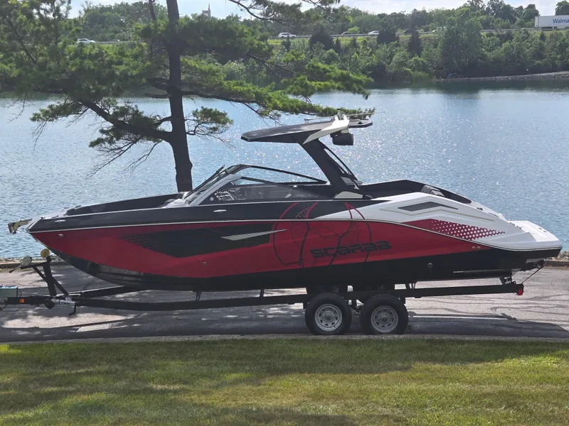 The Image of 2021 Scarab 285 ID boat on trailer by a lake, featuring sleek red and black design. - 0