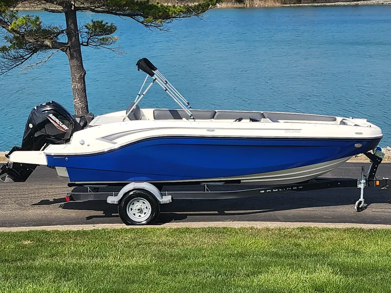 The Image of 2021 Bayliner DX 2000 boat on trailer by a lake, featuring a blue and white design. - 0