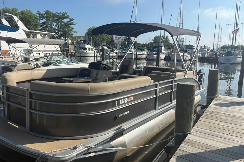 The Image of 2024 Harris HCX23 pontoon boat docked at a marina with surrounding yachts. - 1