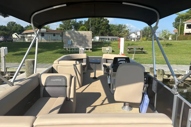 Slide: The Image of 2024 Harris HCX23 pontoon boat interior with seating and helm, docked by grassy area. - 3