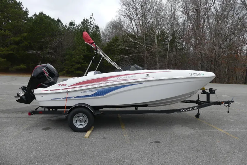 Slide: The Image of 2024 Tahoe T18 boat on trailer in parking lot, surrounded by trees. - 2
