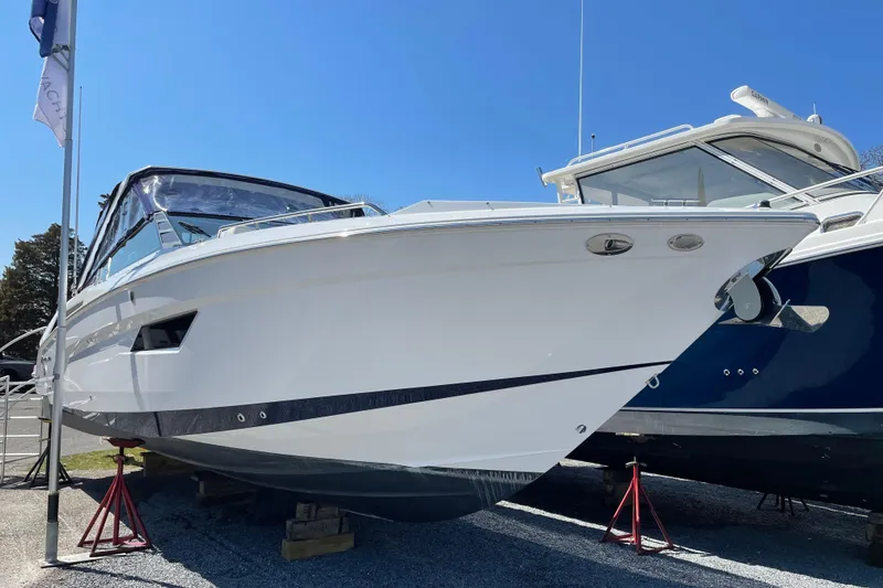 Slide: The Image of 2021 Cruisers Yachts 338 Outboard, white hull, displayed on stands, clear blue sky background. - 2