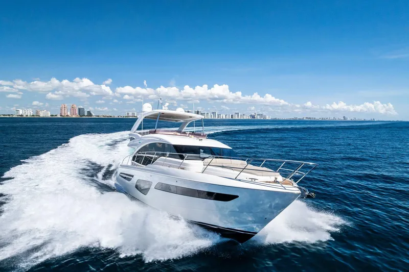 Slide: The Image of 2022 Princess 55 Flybridge yacht cruising on open sea with city skyline in background. - 62