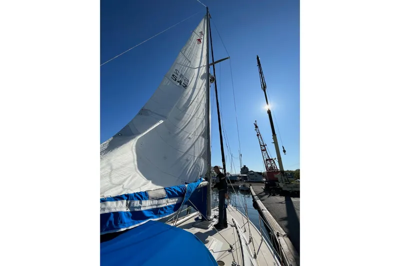 Slide: The Image of 1985 Catalina 36 sailboat with raised sails docked near cranes under clear blue sky. - 2