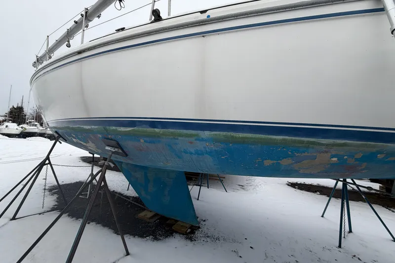 Slide: The Image of 1985 Catalina 36 sailboat on stands, hull showing wear, in snowy boatyard. - 49