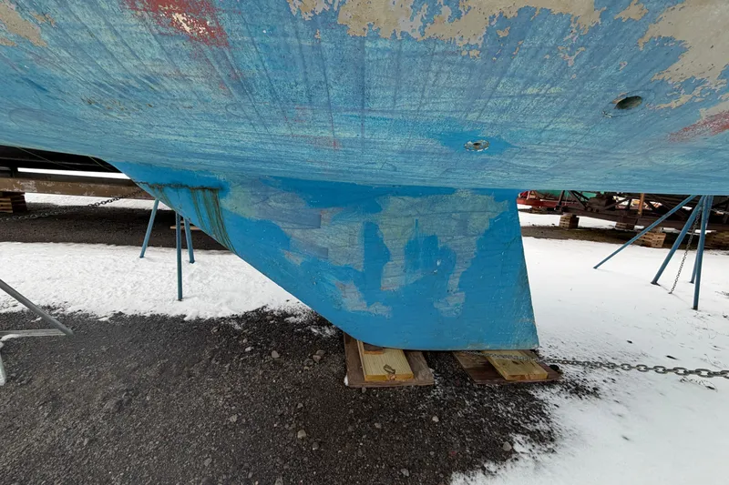 Slide: The Image of 1985 Catalina 36 sailboat hull with peeling blue paint, supported on stands in a snowy yard. - 58