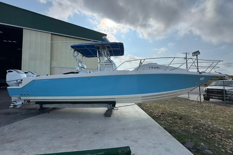 The Image of 1996 Pro-Line 3400 Cuddy boat with blue hull, parked near a warehouse. - 0