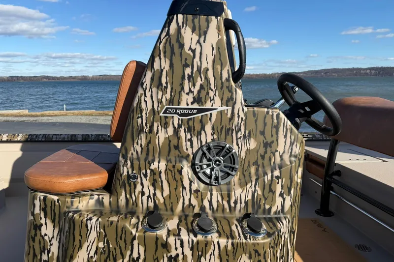 Slide: The Image of 2026 Avid 20 ROGUE CC boat with camouflage design, steering wheel, and seating by the water. - 9