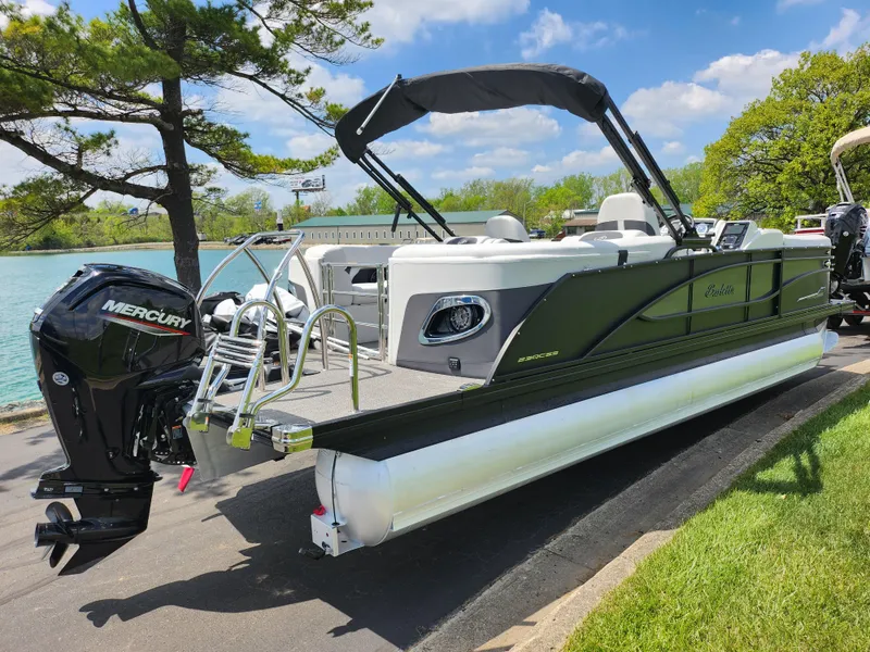 Slide: The Image of 2021 Barletta CORSA 23QC pontoon boat with Mercury engine, docked by a scenic lake. - 1