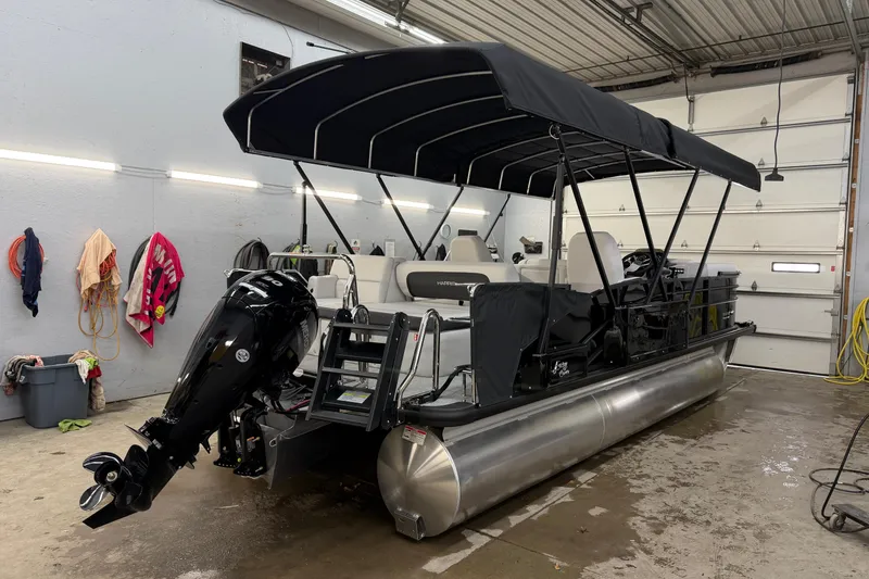 Slide: The Image of 2026 Harris Cruiser 210 pontoon boat in a garage, featuring a black canopy and outboard motor. - 13
